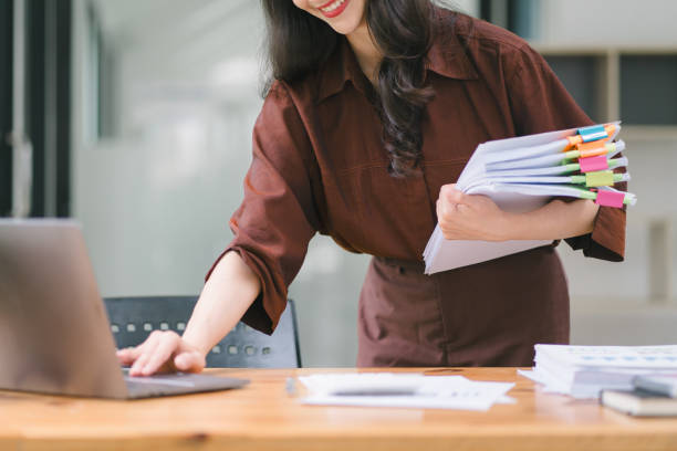 ausgeschnittene aufnahme einer sekretärin, die papierkram trägt und einen laptop im büro benutzt. - stack paper document file stock-fotos und bilder