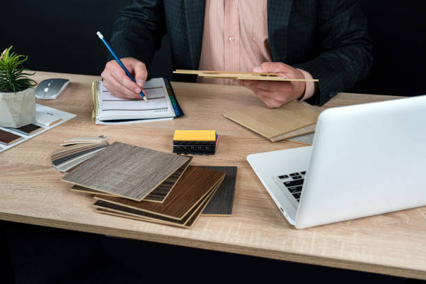 istock Designer hand choosing wood texture laminate  in catalog at office desk, laptop pen and notepad 1696649321