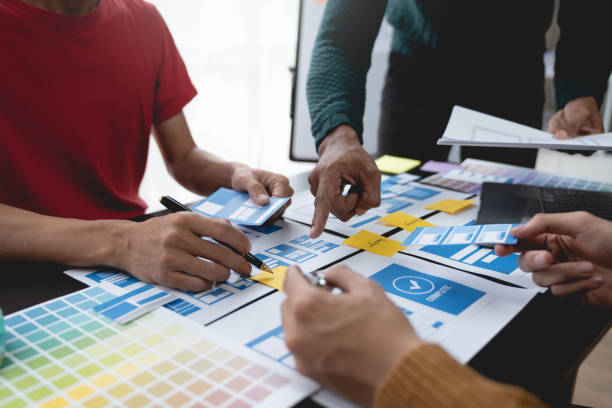 istock ux developers, UI designers Asian group data researchers brainstorm on tabletop mobile app interface wireframe design client summary color codes modern office Creative Digital Development Agency. 1696684935