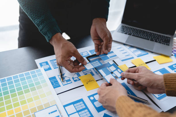 istock ux developers, UI designers Asian group data researchers brainstorm on tabletop mobile app interface wireframe design client summary color codes modern office Creative Digital Development Agency. 1696686075