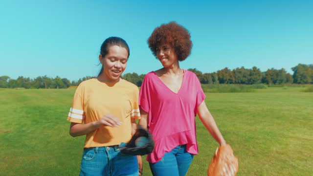 Cheerful teenage daughter and black mother going to play baseball outdoors