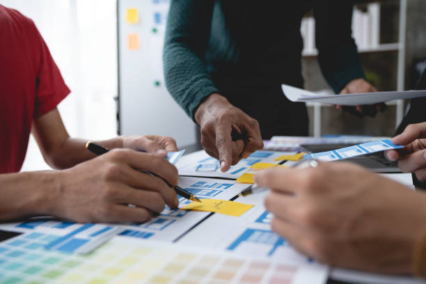 istock ux developers, UI designers Asian group data researchers brainstorm on tabletop mobile app interface wireframe design client summary color codes modern office Creative Digital Development Agency. 1696690320