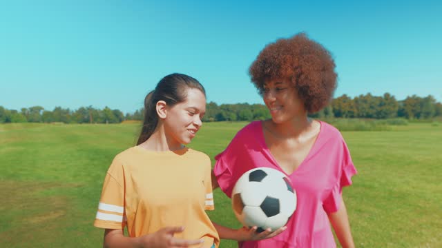 Happy active multiracial family with soccer ball walking along green field