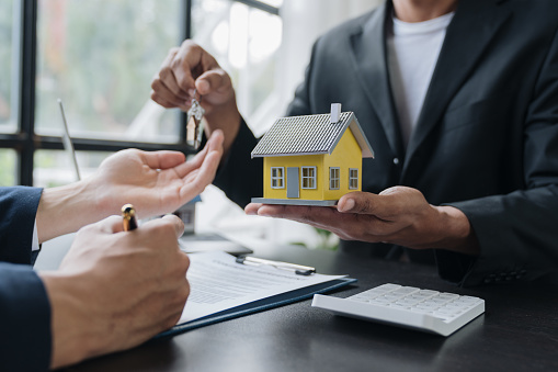 Real estate agents, insurance sales agents, and young Asian businessmen handing home keys and model homes to homebuyers after signing sales contracts are satisfied in the office.