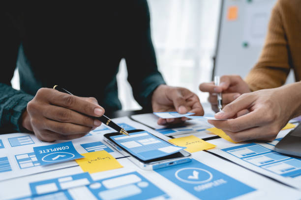 istock ux developers, UI designers Asian group data researchers brainstorm on tabletop mobile app interface wireframe design client summary color codes modern office Creative Digital Development Agency. 1696699166