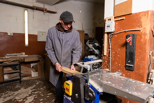 A craftsman works on woodworking machines and saws in a furniture workshop