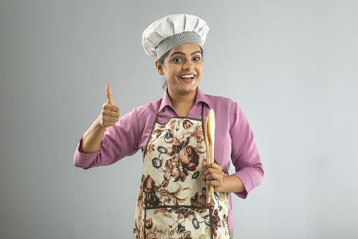 Portrait of smiling female chef showing OK sign while standing on white background