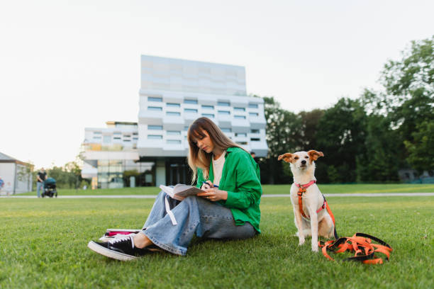 The beautiful female student makes some notes while studying sitting on the grass in the campus background