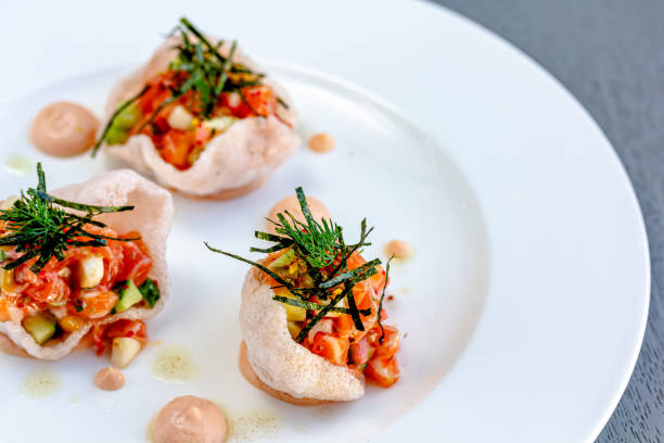 Salmon tartare with tomato, red onion, garlic, basil, capers, lotus root, tobiko caviar, lemon, chives. Isolated on black background