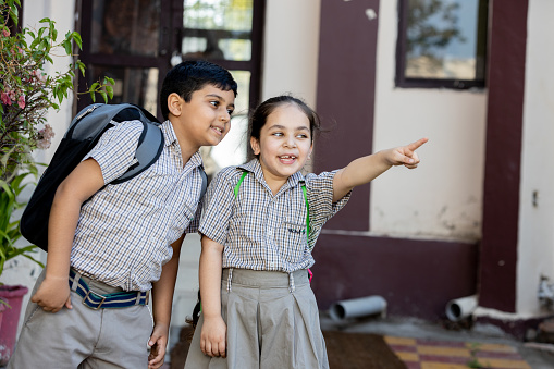 Happy indian school kids student pointing at something outside the primary school looking at camera. Education concept.
