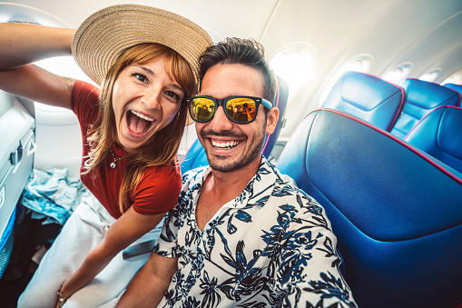 Happy tourist taking selfie inside airplane - Cheerful couple on summer vacation - Passengers boarding on plane - Holidays and transportation concept