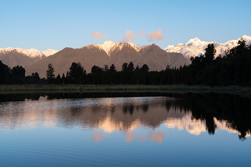 Evening descends upon Lake Matheson, on New Zealand's South Island, and the spectacular Southern Alps are lit up by the setting sun.