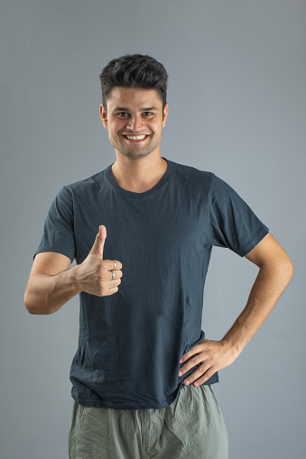 Portrait of handsome young man giving thumbs up while standing against gray background