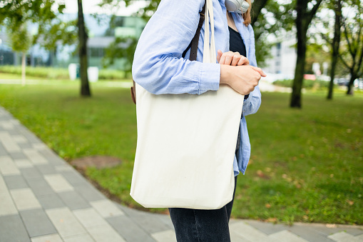 Stylish woman holding white blank canvas tote shopping bag outdoor. Empty reusable canvas tote bag mockup for design. High quality photo