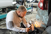 The mechanic uses welding to repair a damaged car.