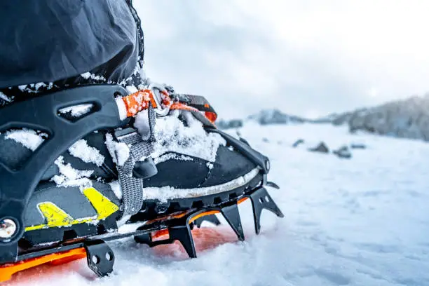 Foot with crampon on boot standing on winter mountain snow