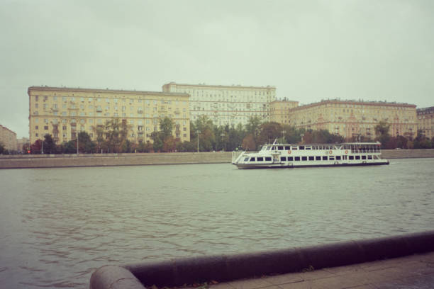 Moscow, Russia - May 17, 2025: A river tram sails from Filevsky Park along  Moscow River past the Red Bridge on  cloudy spring day, demonstrating  unity of nature, transport, architecture, and urban space.