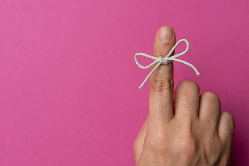 Hand and string tied on index finger on pink background.