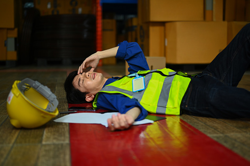 Asian male worker lying down on floor with injured head after accident in a warehouse.