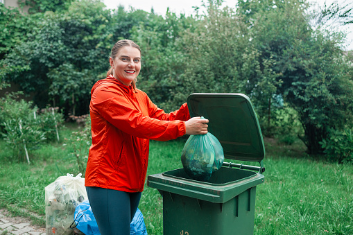 Caucasian woman sorting garbage, throwing a used paper bag in a small recycle bin at outdoor near a home . High quality photo