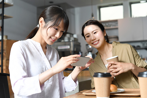 Smiling young Asian women taking pictures of food with smartphones at a cafe