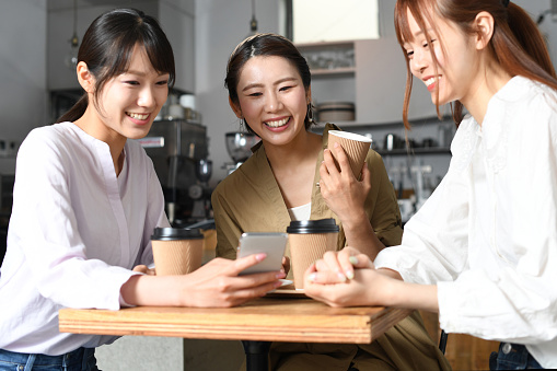 Smiling young Asian women having fun while looking at their smartphones at a cafe