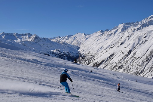 Skiers and snowboarders in Hochgurgl ski resort, backdropped by the Ötztal valley and the snow capped alpine mountains in Tyrol, Austria on a beautiful sunny day, perfect conditions for winter sports.