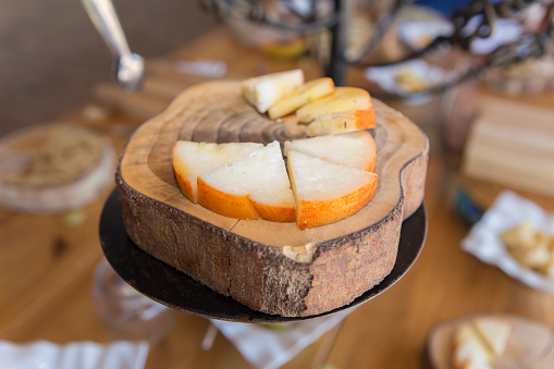 Half-cured smoked paprika cheese slices displayed over tree bark tray. Closeup