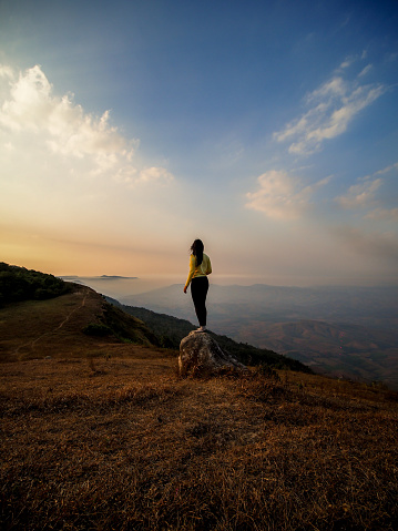 Alone tourist on the edge of cliff and watching into deep valley bellow at Phu Bak Dai, Loei, Thailand. A tourist woman stand alone at the cliff of mountain to see scenic view of sunset and range of mountain.