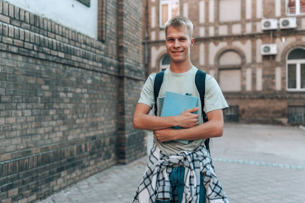 istock Male student holds notebooks outside university 1696897509