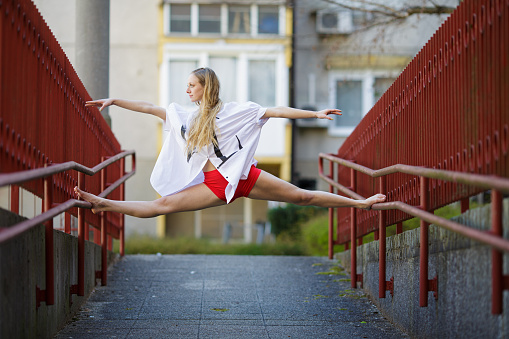 Young woman in a dance pose on a stairs railing in an urban city.