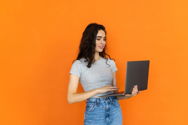 istock Young smiling freelancer copywriter student woman hold laptop browsing on yellow orange background 1696920825