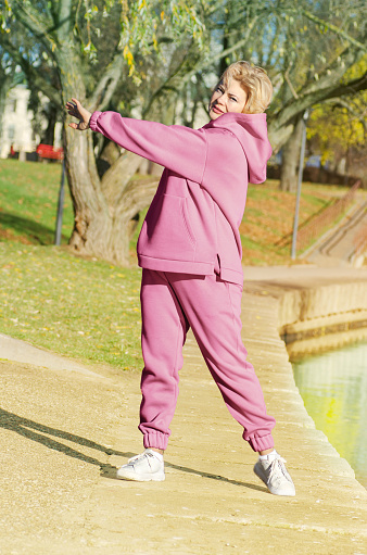 Mature woman in pink hoodie doing sports in autumn park.