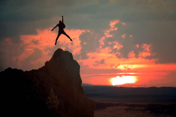 A silhouette of a woman standing on the edge of a cliff,  in the \