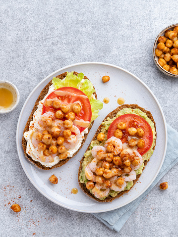 Healthy snack, lunch or breakfast, toasted rye breadwith avocado, tomatoes, cream cheese, shrimps and chick peas in spices.