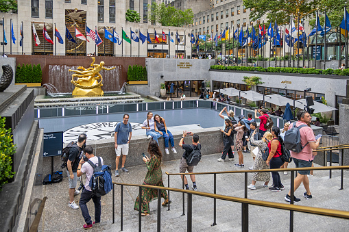 Rockefeller Center, Manhattan, New York, USA - August 8th 2023:  Tourists taking photographs of each other in front of the fountain and statue in front of the center and famous sky scraper