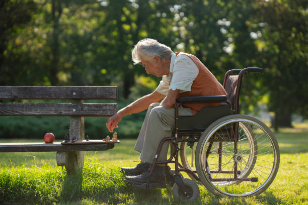 starszy mężczyzna na wózku inwalidzkim z szachami na ławce jest sam w miejskim parku, czując się samotny. - arthritis senior adult rheumatoid arthritis sadness zdjęcia i obrazy z banku zdjęć