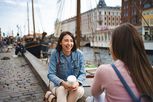Two female friends catching up over coffee while sitting by the Nyhavn canal in the center of Copenhagen