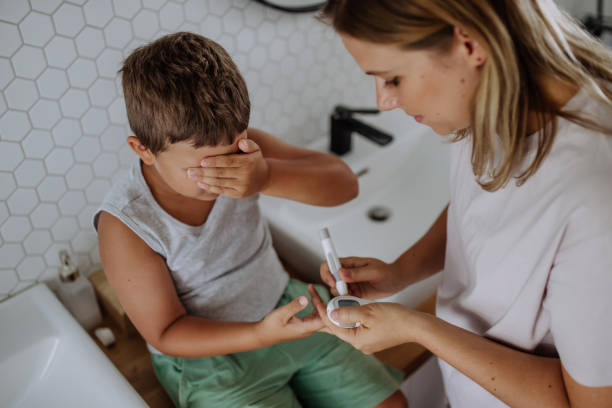 自宅で指先血糖計を使って息子の血糖値をチェックする母親。 - hypoglycemia diabetes child hyperglycemia ストックフォトと画像
