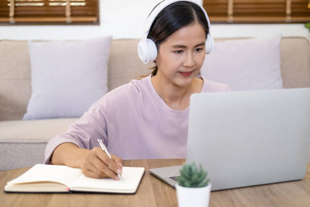 istock Attractive female student learning language, watching online webinar, listening audio course, Focused woman wearing headphones using laptop in cafe, writing notes, e-learning education concept 1697010626