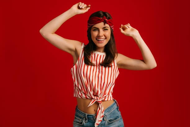 istock Stylish young hipster woman dancing and smiling while standing on red background 1697040585
