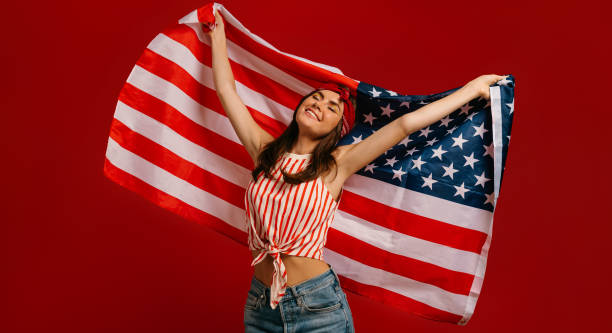 istock Joyful young hipster woman carrying American flag while standing on red background 1697042320