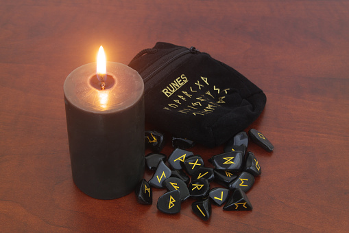 Stone runes with black candle on wooden table.