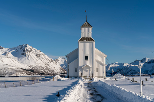 White wooden church and small cemetery in Gimsøy on Gimsoysand island in Lofoten archipelago in snow.