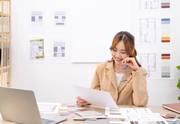 istock Young asian female interior designer or architect working on creative project with drawing, material sample & laptop computer in office. Business of Real estate, home decoration & renovation concept. 1697067157