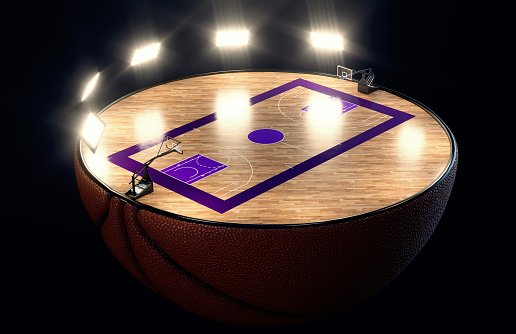 A basketball ball split in half revealing a marked wooden court with hoops at night under illuminated floodlights - 3D render