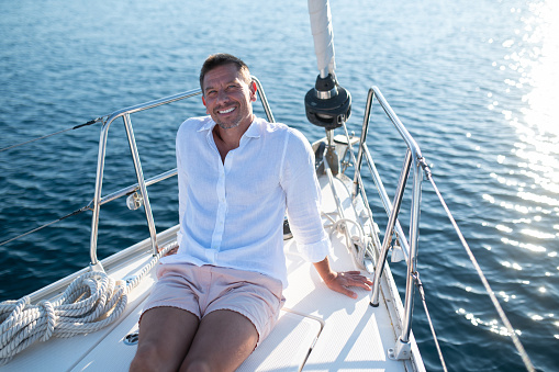 Happy man. Man in white clothes sitting on a yacht deck and looking relaxed and happy