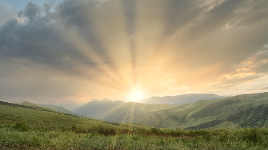 The scenery consists of sunlight shining through the rays of the sun and a beautiful mountain landscape.