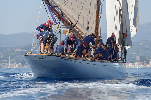 Imperia, Italy - September 10, 2023: Crew members aboard on sailboat Tuiga, flagship of the Monaco Yacht Club, during racing in Gulf of Imperia. Established in 1986, the Imperia Vintage Yacht Challenge Stage is a of the most important event in sailing the Mediterranean dedicated to historical boats
