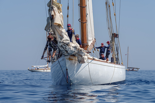 Imperia, Italy - September 10, 2023: Crew members aboard on sailboat Tuiga, flagship of the Monaco Yacht Club, during racing in Gulf of Imperia. Established in 1986, the Imperia Vintage Yacht Challenge Stage is a of the most important event in sailing the Mediterranean dedicated to historical boats